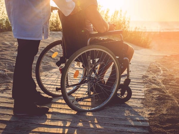 Imagen de una persona con mobilidad reducida en la playa junto a su acompañante)